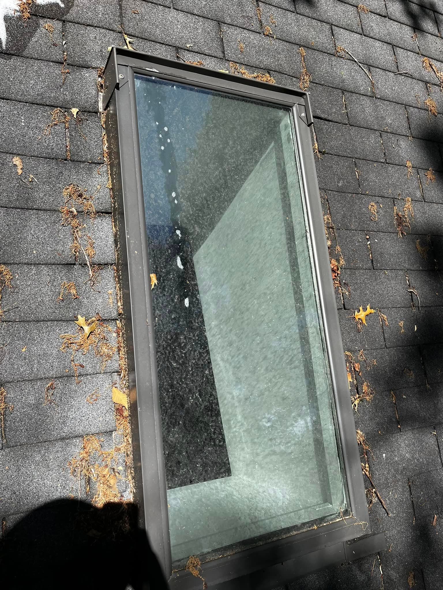 Skylight on a sloped roof with debris and leaves around it.
