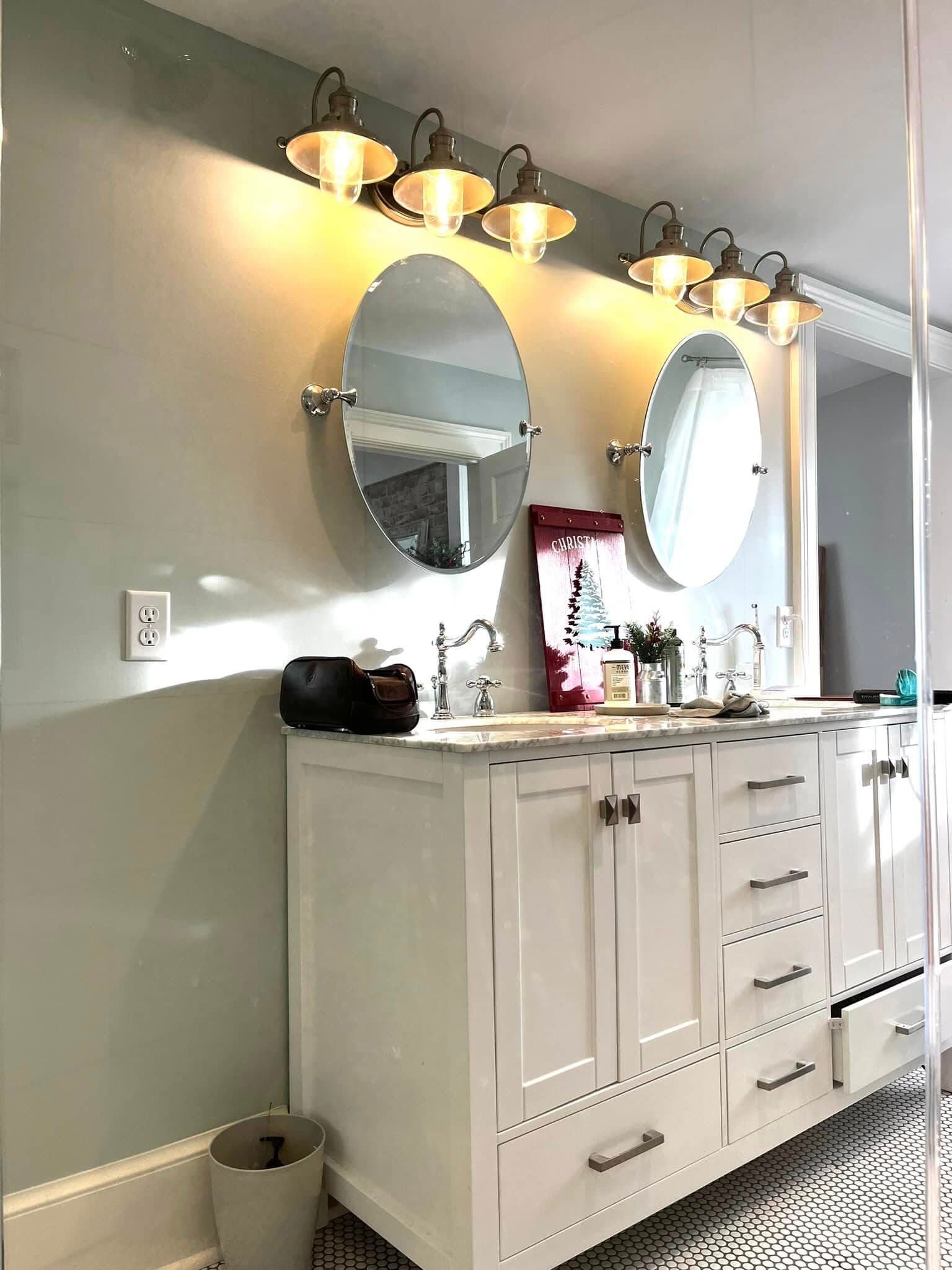 Bright modern bathroom with dual round mirrors, stylish lighting, and white cabinetry.