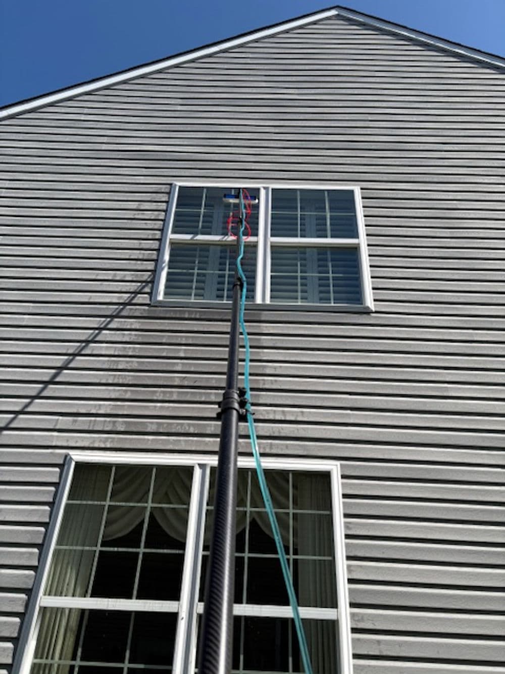 Cleaning equipment reaches high window on a gray house exterior under clear blue sky.
